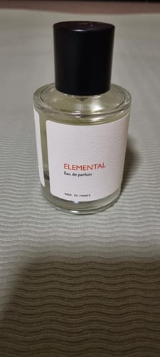 Customer's bottle of Elemental Eau de Parfum in a clear glass bottle with a black cap, set on a textured surface.