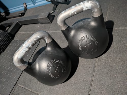 Customer's two black Adjustable Kettlebells on a gym floor, with visible wear on the handles from use.