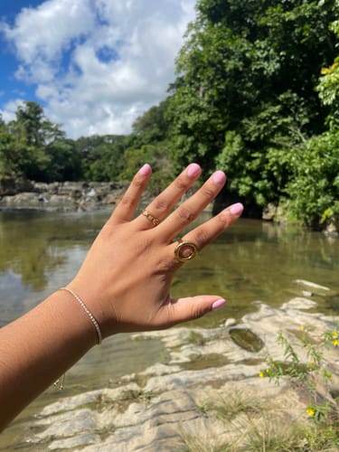 Customer's hand wearing the gold Isabella Chain Ring on their middle finger with a river in the background.