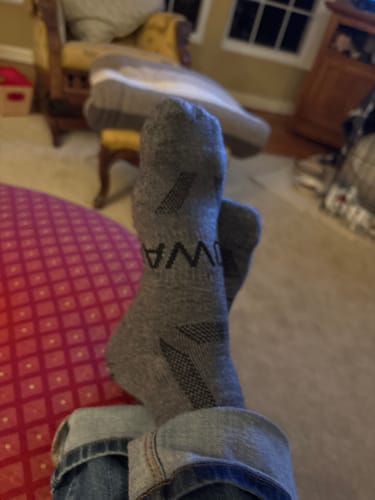 Close-up of a reviewer's feet propped up, wearing the grey Men's Alpaca Socks indoors.