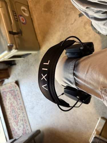 Customer's black TRACKR™ Electronic earmuffs resting on their leg, with the AXIL logo visible on the headband.
