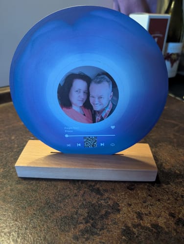 Kunde zeigt die personalisierte Acryl-Schallplatte. Die blaue Platte mit Foto steht auf dem hölzernen Aufsteller.