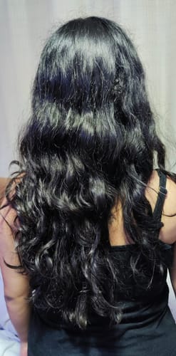 Reseñadora mostrando la parte de atrás de su cabello largo y oscuro con rizos definidos gracias al Activador de Rizos.