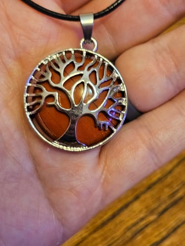 Reviewer holding a crystal necklace with a silver-colored tree pendant over a round, orange stone.