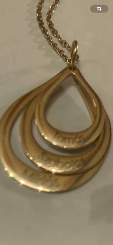 Close-up of a customer's gold Celestial Necklace showing the engraved names on its nested teardrop pendants.