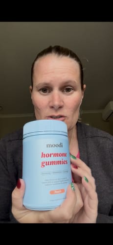 Reviewer holding up a light blue container of Moodi hormone gummies, showing the Peach flavor.