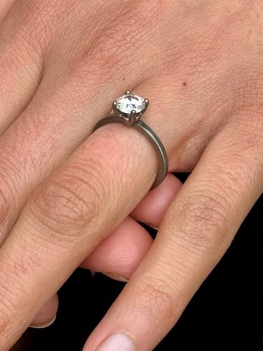 Reviewer's hand wearing The Athena engagement ring, showing the simple brushed titanium band and round moissanite stone.