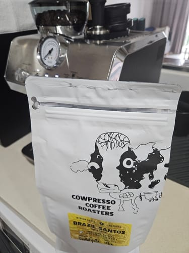 Customer's pouch of Brazil Santos coffee on a counter in front of an espresso machine.