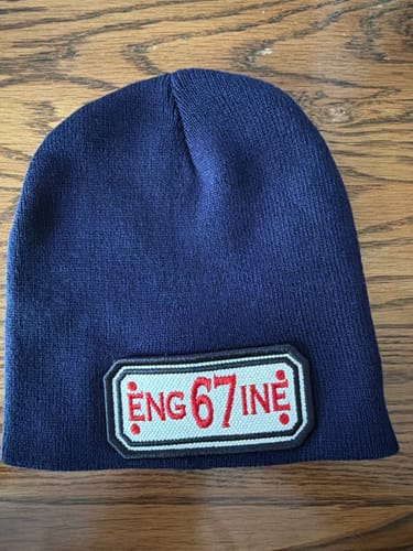 Customer's navy blue Custom Hose Skull Cap with a white patch reading 'Eng67ine' in red, laid on a wood surface.