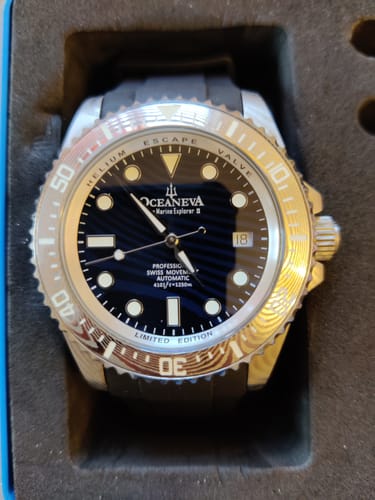 Reviewer's close-up of the Oceaneva watch, highlighting the blue Damascus steel dial and silver bezel inside its case.