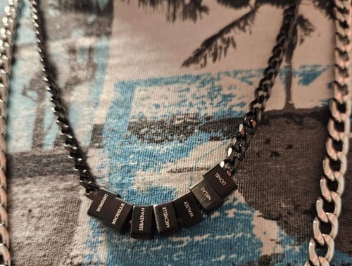 Customer's black Legacy Necklace with multiple beads personalized with names, resting on a patterned t-shirt.