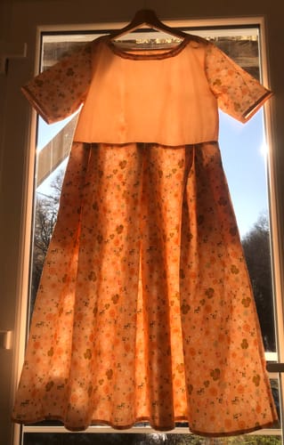 Robe Louise d'une cliente en tissu orange à motifs, avec des manches courtes et un corsage uni.
