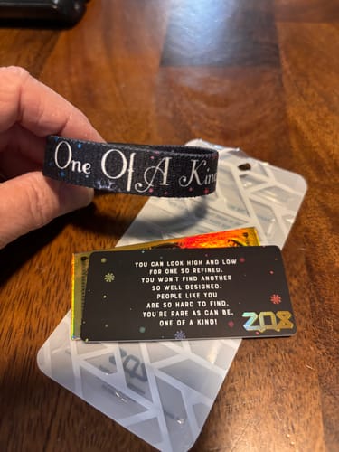 Reviewer holding the black 'One Of A Kind' bracelet, showing the elegant white script.