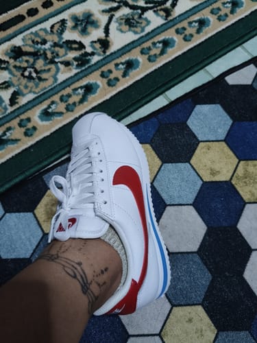Customer's foot wearing the white Nike Cortez Leather shoe, showing the red swoosh and blue midsole.