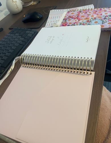 Customer's 2026 Signature Planner with gold spiral binding, open on a desk to the blush pink inside cover.