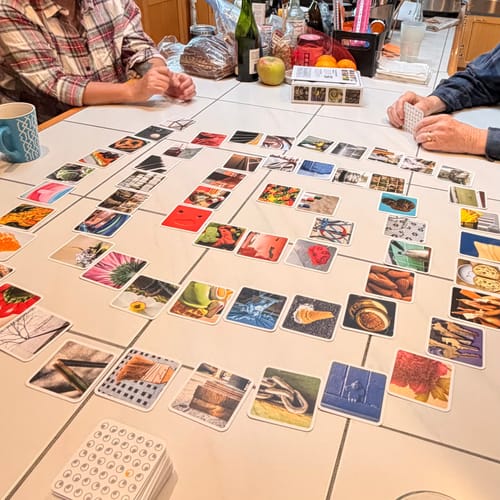 Customers playing the OuiSi Original card game at a table, with photo cards laid out in a large, connecting pattern.