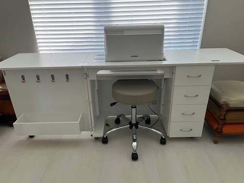 Reviewer's fully assembled white Harriet Sewing Cabinet with side leaves extended and a sewing machine placed in the hydraulic lift.