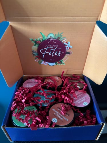 Client montrant le Coffret de Noël ouvert, rempli de pots de beurre et chantilly sur un lit de papier de remplissage rouge.