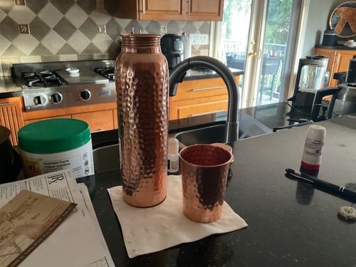 Customer's hand-hammered Himalayan Ayurvedic Pure Copper Bottle and a matching cup on a kitchen countertop.
