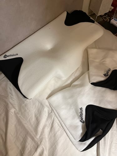 Cliente montrant ses filets de lavage Cellsius sur un lit à côté d'un oreiller orthopédique blanc et noir.