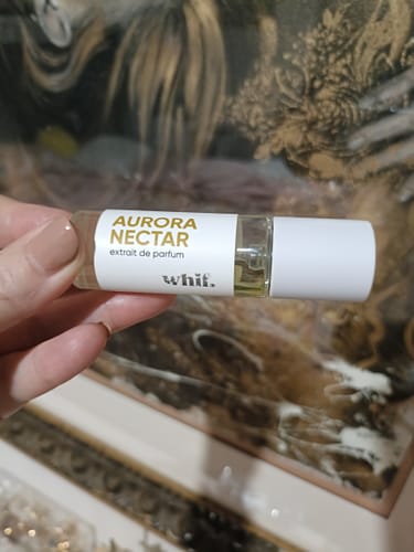 Customer's hand holding the mini-size Aurora Nectar perfume bottle against a blurred background.