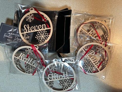 Customer's five personalized wooden Christmas ornaments with snowflake designs, individually wrapped in clear bags.