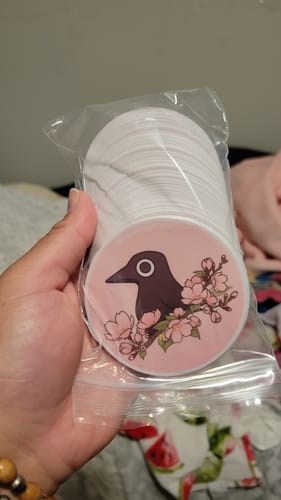 Customer holds a bag containing a stack of custom round stickers with a bird and cherry blossom design.