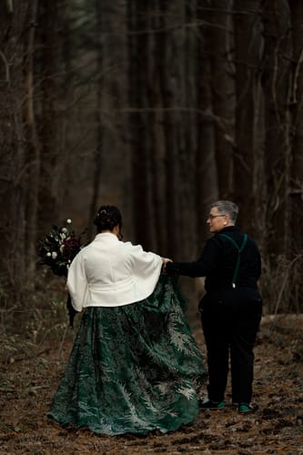 Customer seen from behind wearing the green patterned Pine Glimmer Flair Gown with a white jacket in a forest.