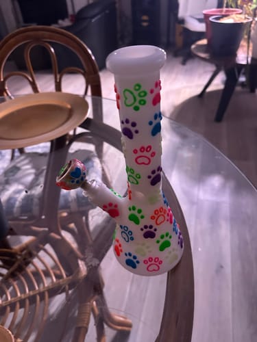 Customer's Glow in the Dark Paws Beaker Bong with bright, colorful paw prints standing on a glass table.