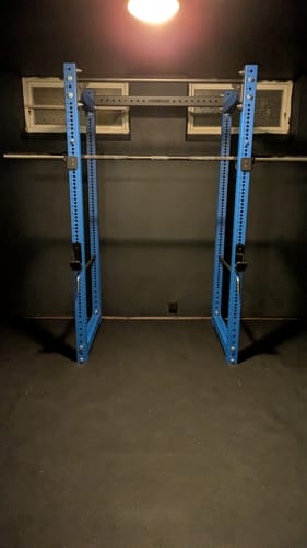 Customer's blue Riot MRR 75 power rack assembled with a barbell in a dimly lit home gym.