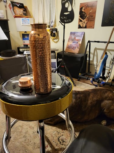 Customer's hammered Himalayan Ayurvedic Pure Copper Bottle and its lid sitting on a stool in a room.