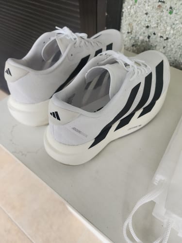 Reviewer's pair of white adidas Adizero EVO SL running shoes with black stripes on a counter.