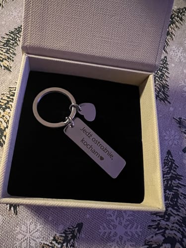 Rezensent zeigt einen gravierten Schlüsselanhänger mit Herz-Charme in einer Geschenkbox.