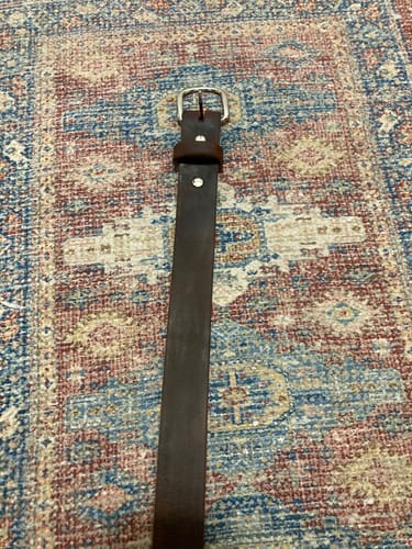 Customer's dark brown Crazy Horse belt with a silver buckle laid out straight on a patterned rug.