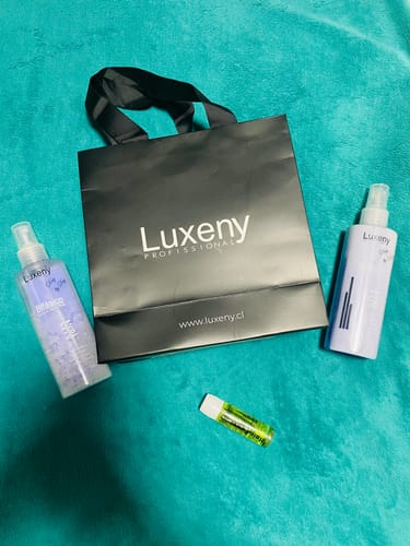 Una clienta muestra su compra de Luxeny, incluyendo el Spray Bifásico, sobre una superficie verde azulado.