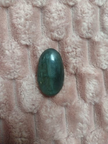 Customer's dark green labradorite palm stone resting on a fuzzy pink surface.