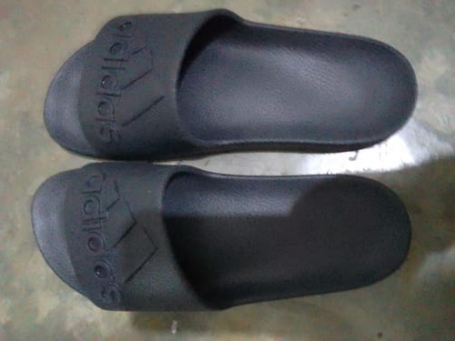 Customer's pair of all-black adidas Adilette Aqua Slides shown from an overhead perspective on the floor.