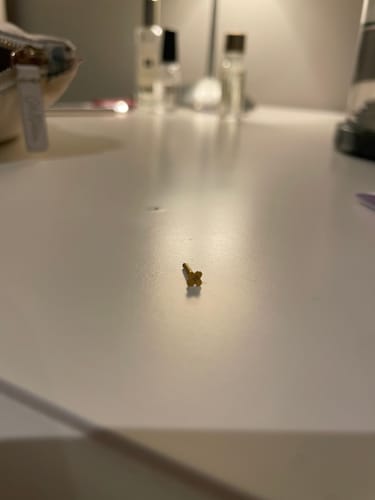 Reviewer's close-up of the Solitaire flatback Gold, showing the cross-shaped back on a white surface.