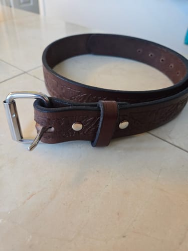 Customer's dark brown The Gunner Eagle belt, coiled on a tile surface, showing the embossed pattern and silver buckle.