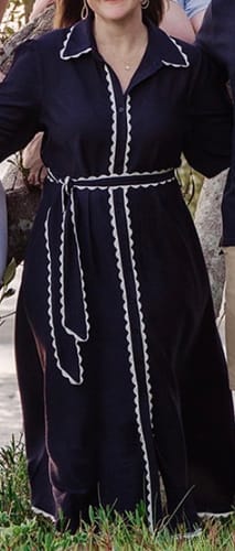 Customer wearing the navy Shyla Dress with white scalloped trim and a matching tie-waist belt outdoors.