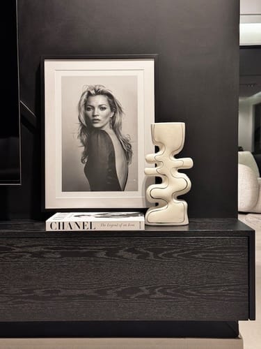 Reviewer's white ceramic vase with black detail displayed on a dark wood console table next to a framed photo.