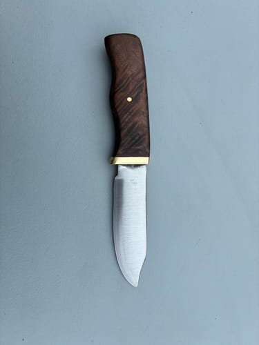 Reviewer's finished knife with a dark, figured wood handle and a satin blade, laid on a grey surface.