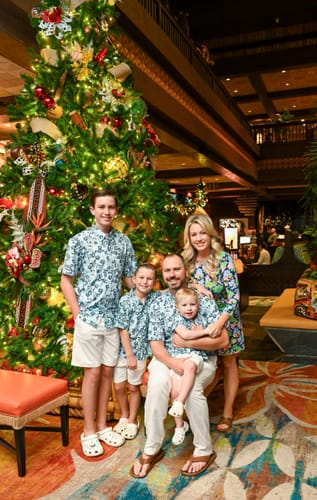 Customer's husband and three sons in matching light-blue Aloha Pal shirts posing for a family photo by a Christmas tree.