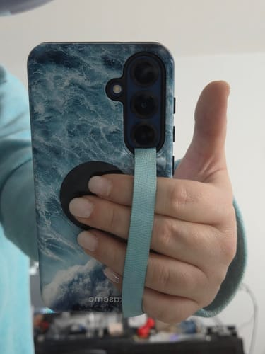 Customer holding their phone by a light blue strap attached to the stylish Summer Break case with an ocean wave design.