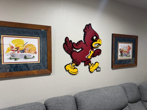A reviewer's Iowa State Cyclones 'CY' 3D metal wall art mounted on a wall above a grey couch, between two framed pictures.