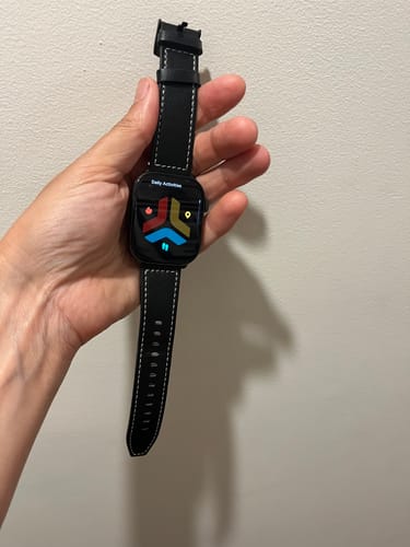 Reviewer holding a smartwatch with the black leather strap with white stitching.