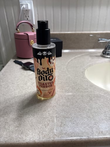 Reviewer's bottle of Toasted Terror Body Oil sitting on a bathroom counter next to the sink.