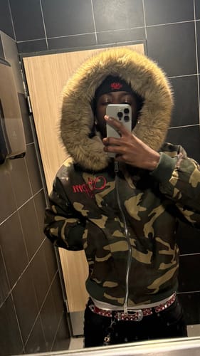 Customer takes a mirror selfie wearing the camouflage Embroidered Hooded Jacket, highlighting the large faux fur hood.