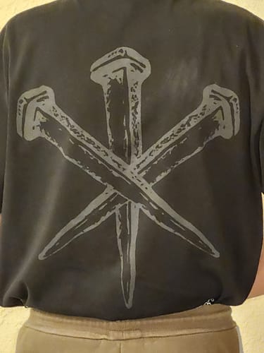 Reviewer showing the back of the black Romans 6:23 Three Nails T-Shirt, highlighting the large nails graphic.