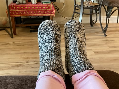 Reviewer relaxing with their feet up, wearing the speckled Gripper Slipper Booties pulled up tall over pink pants.